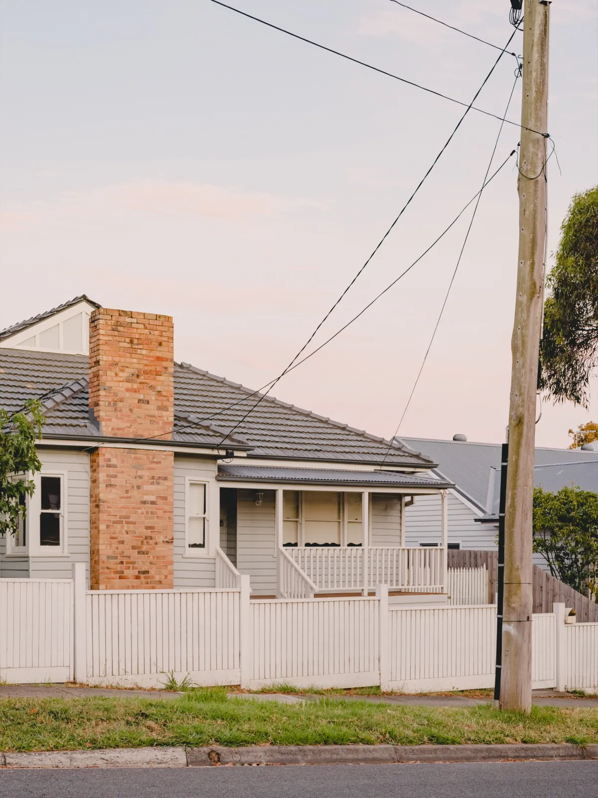 Street view of the weatherboard Burwood East home with a feature brick chimney, picket fence, and gabled roof.