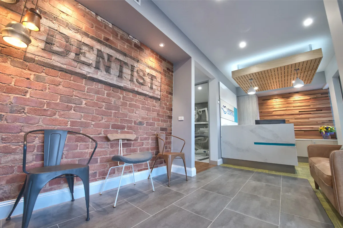 Reception with exposed-brick DENTIST signage, slat-timber feature ceiling, and grey-tiled floor.
