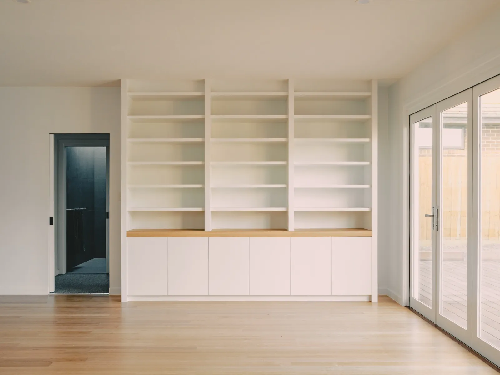 Living room with white built-in bookshelves over base cabinets with a timber benchtop, French doors, and a dark internal door.