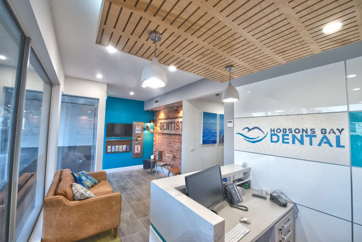Reception at Hobsons Bay Dental with HOBSONS BAY DENTAL mosaic signage and a slat-timber feature ceiling.