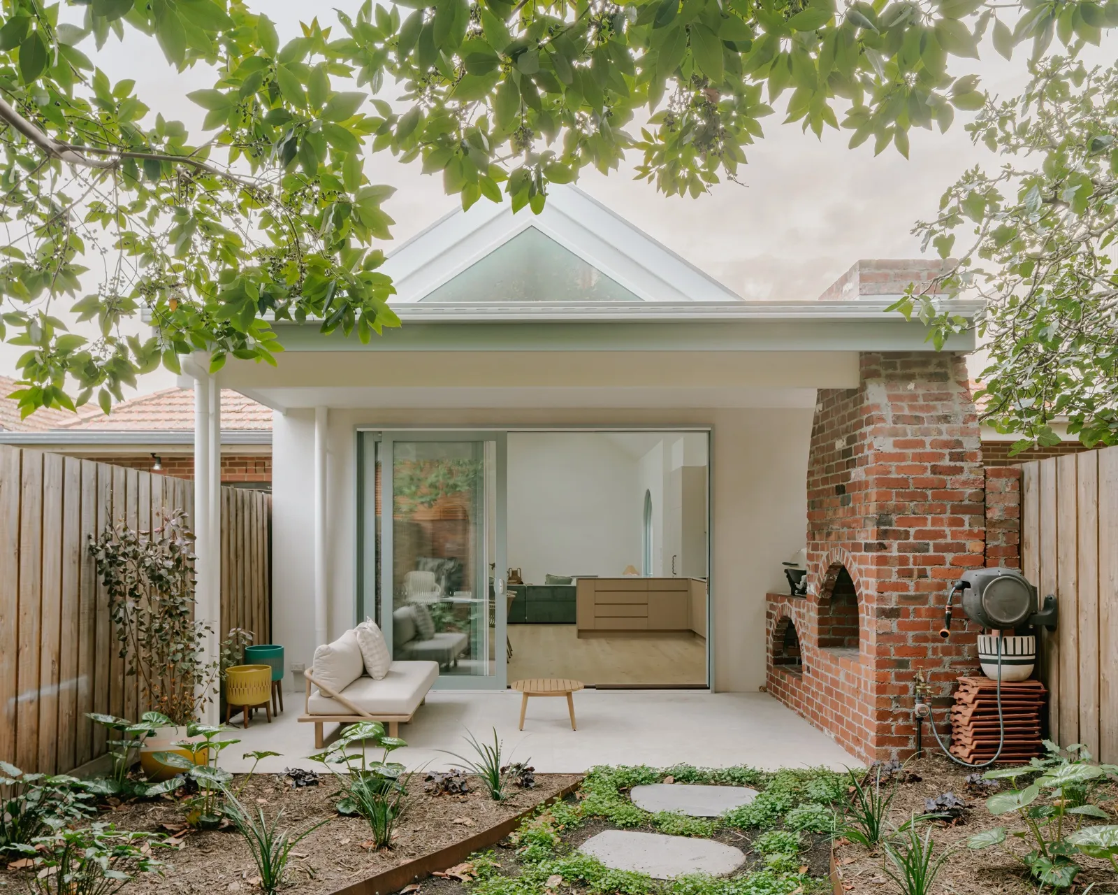 Rear extension with gabled glazing, sliding doors to a paved courtyard, and a retained red-brick chimney with timber fence backdrop.