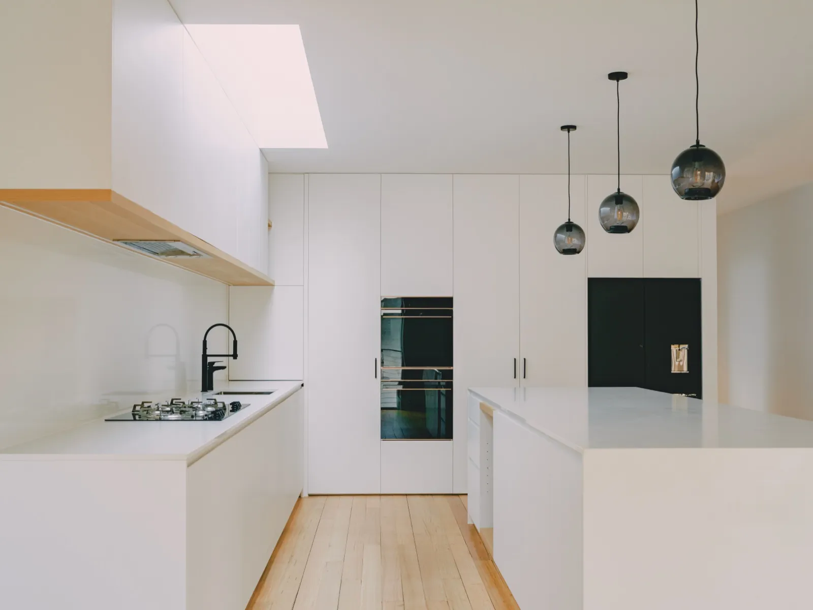 Burwood East kitchen with white cabinets, gas cooktop, integrated wall ovens, and three smoke-glass pendants over the island.