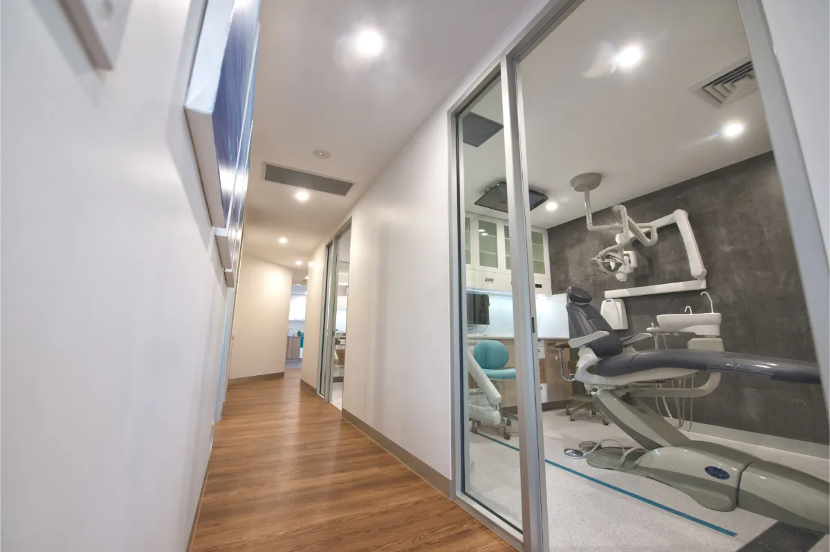 Corridor view to dental surgery with timber floor and glass-walled treatment room.