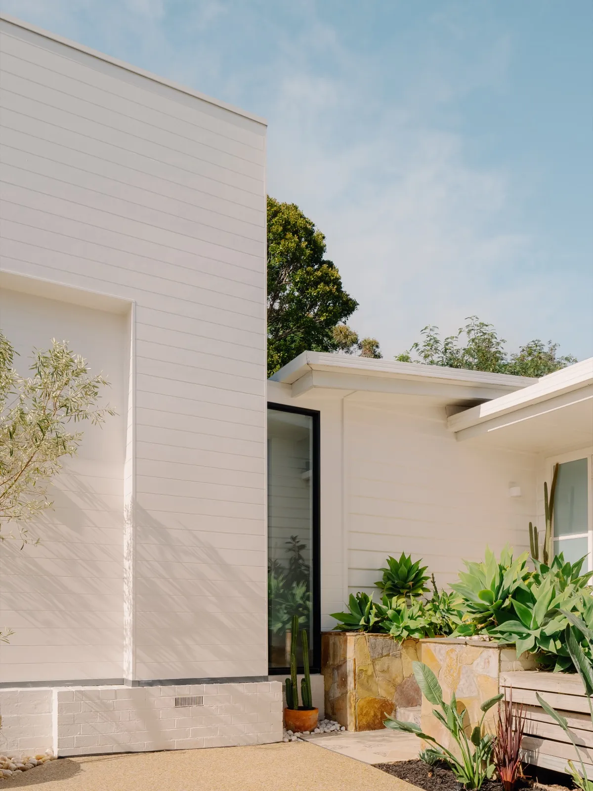 Front of the home with rendered brick base, white cladding, and stone planters filled with succulents.