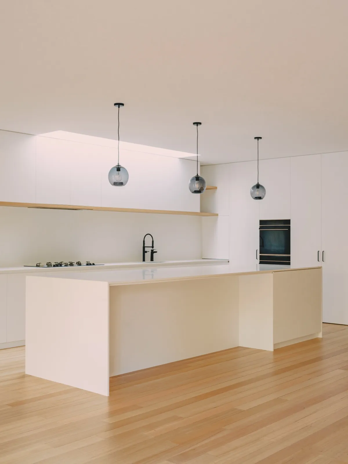 Kitchen island with white stone benchtop, gas cooktop along the rear wall, and three smoke-glass orb pendants on black cords.