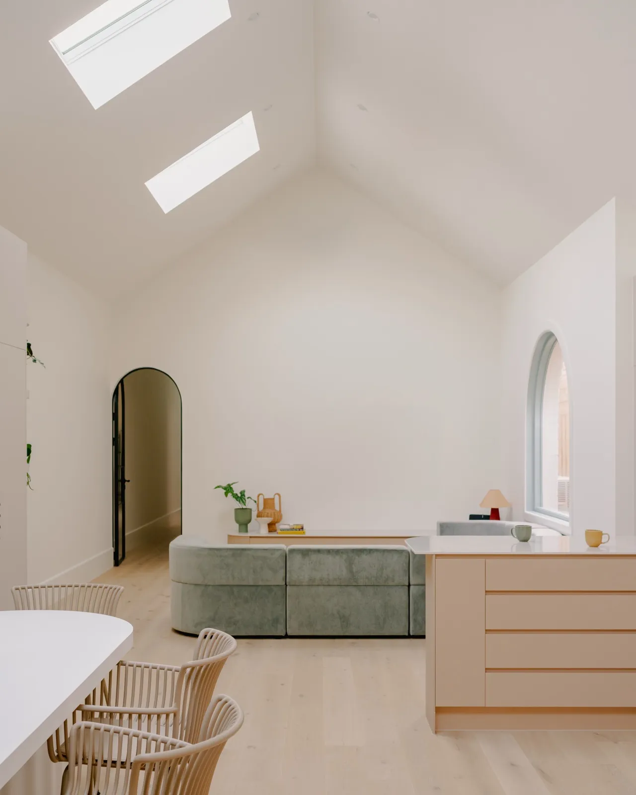 St Kilda living and dining room with vaulted ceiling, twin skylights, blush kitchen island, arched window, and a curved sage velvet sofa.