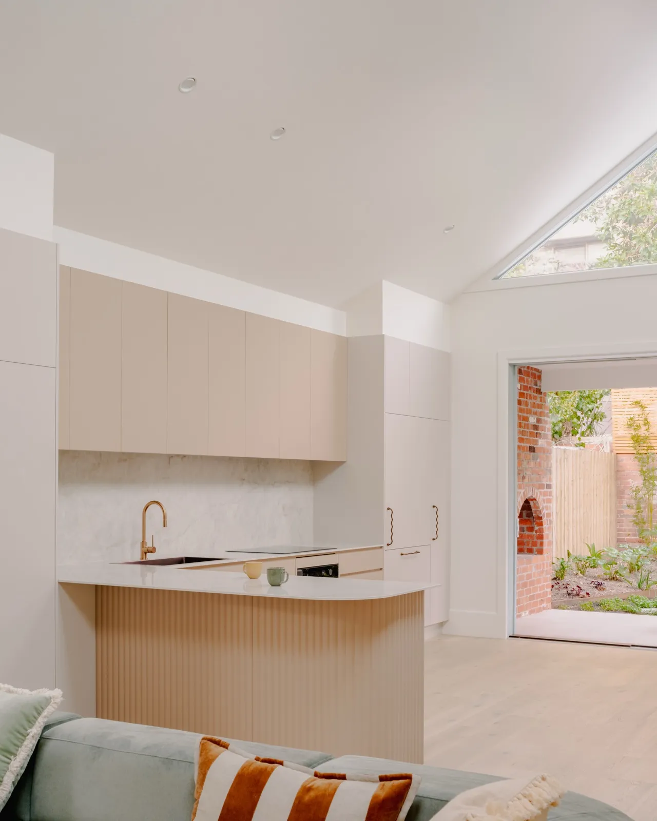 Living room view of the blush galley kitchen with fluted island base and a triangular gable window over the rear courtyard.