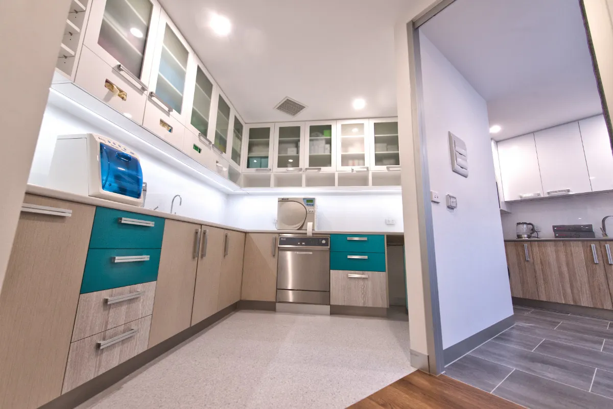Sterilisation room with white cabinetry, teal accent drawers, and overhead glass-front cabinets.