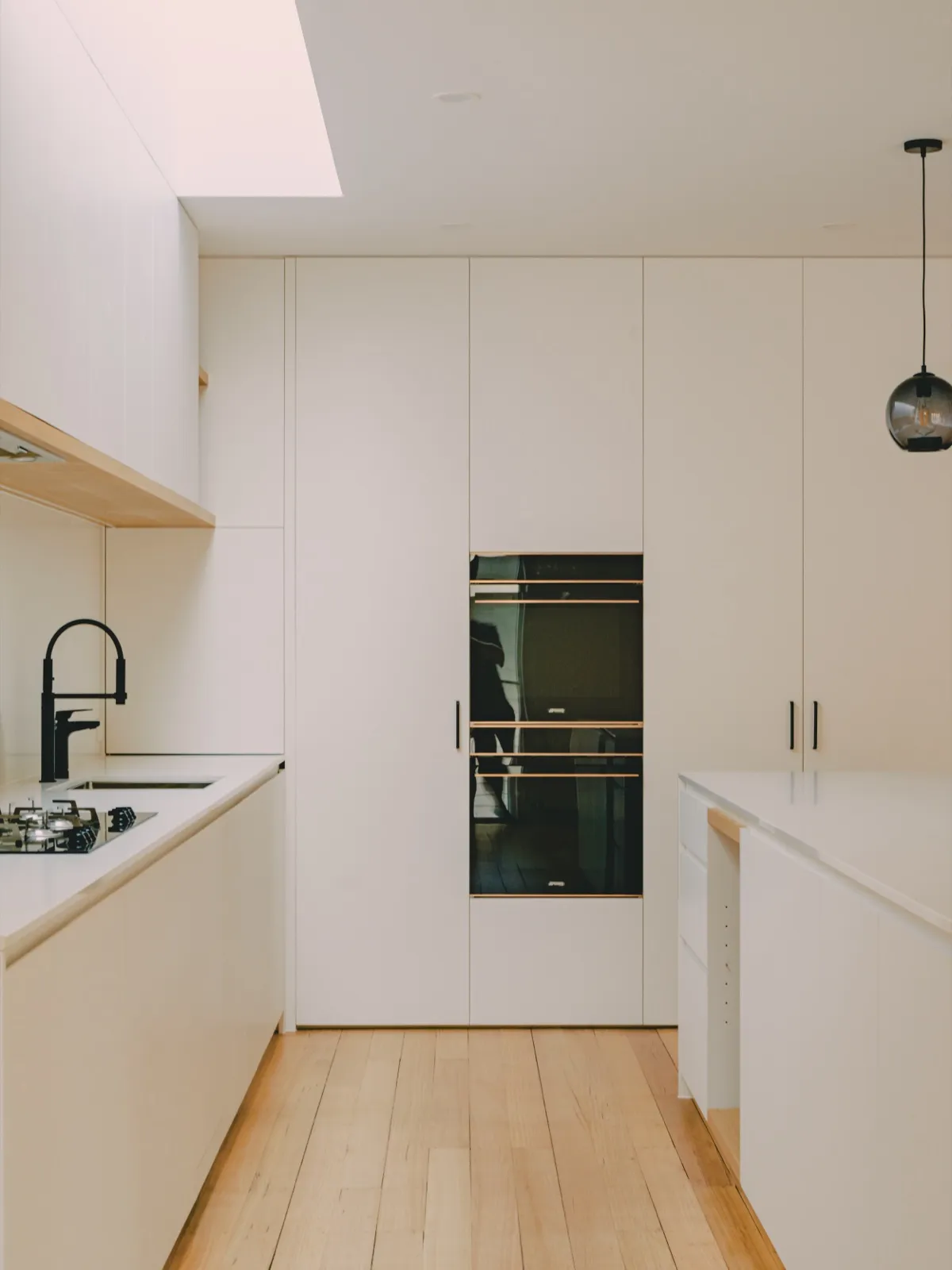 Tall white cabinetry with a built-in Smeg wall oven and warming drawer, beside the gas cooktop and a smoke-glass pendant.