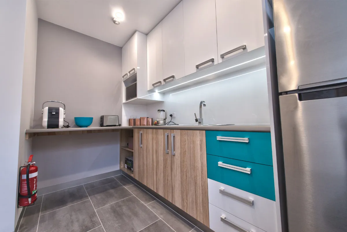 Staff kitchen with white upper cabinets, teal accent drawers, and stainless fridge.