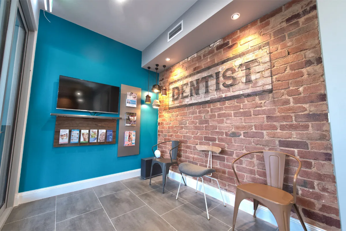 Waiting area with painted exposed-brick DENTIST sign, teal accent wall, and wall-mounted TV.