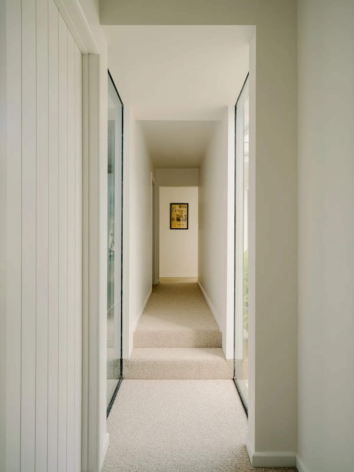 Internal corridor with framed glass walls, neutral carpet, and a small framed artwork at the far end.