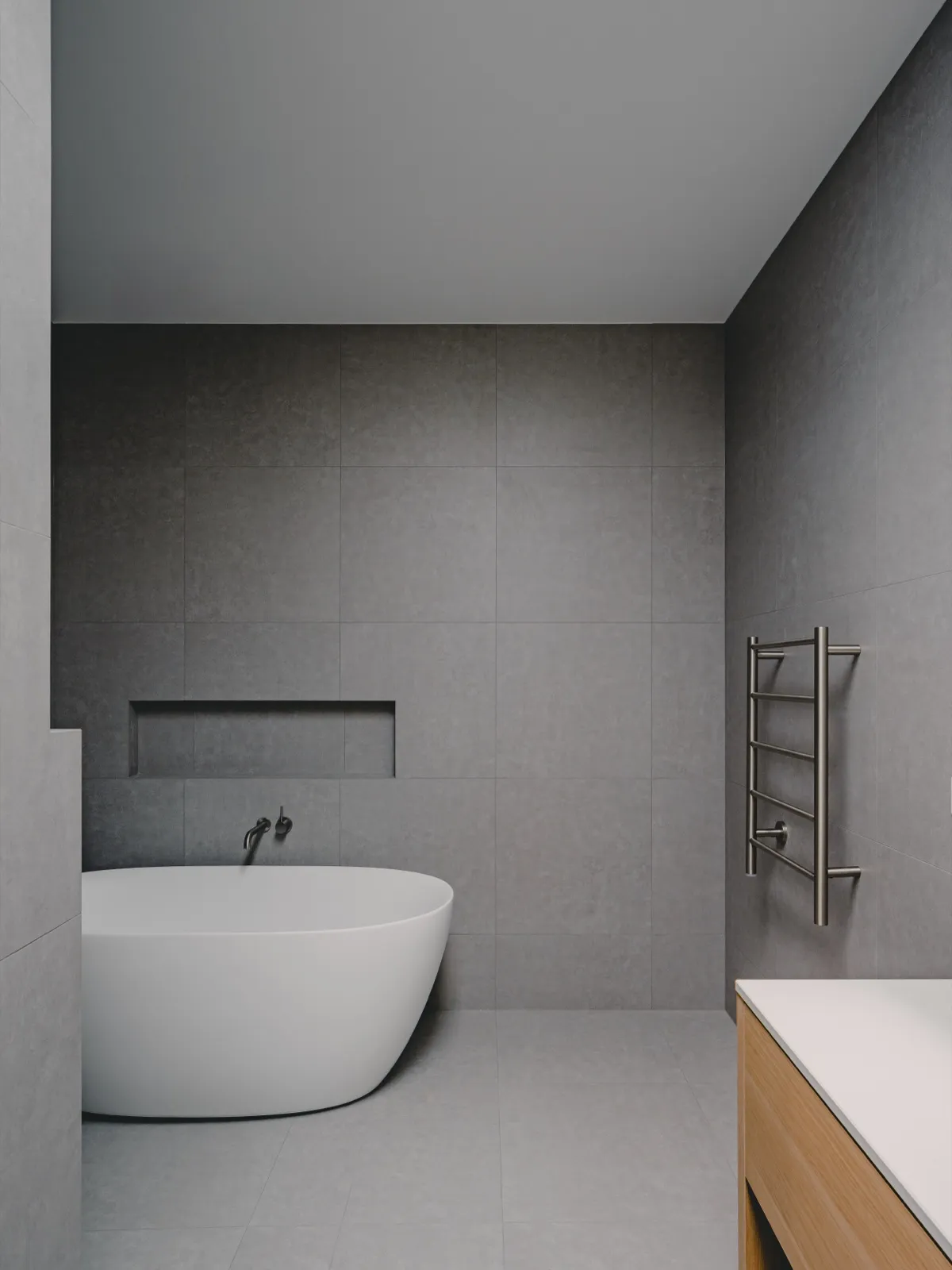 Bathroom with grey stone-look feature tiles, freestanding white tub, recessed niche, brushed nickel towel rail, and timber vanity.