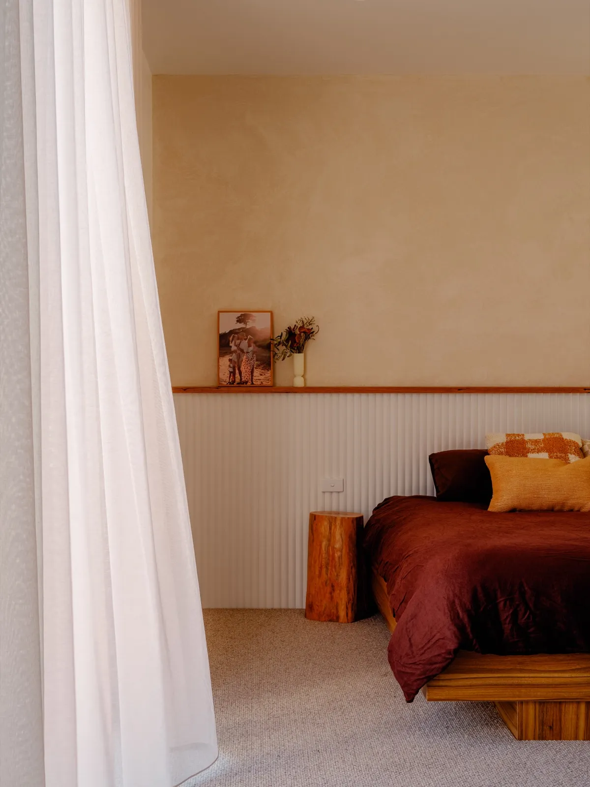 Bedroom with burgundy linen, timber bedframe, vertical-panelled wainscot, and a sheer curtain beside a stump side table.