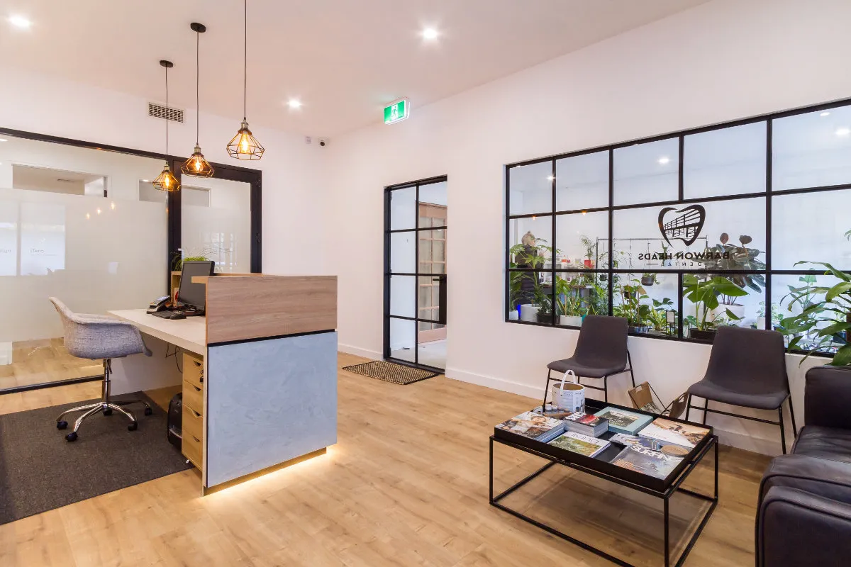 Reception desk and waiting area with steel-framed glazing, pendant lights, and a timber floor.