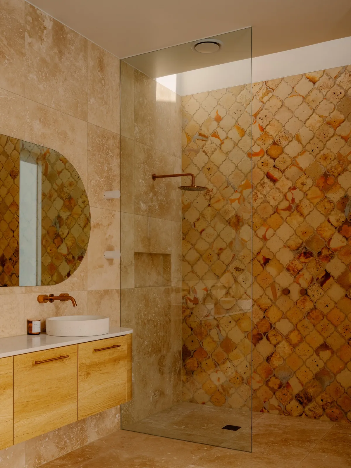 Travertine bathroom with arabesque feature tile, walk-in shower, round mirror, and floating timber vanity with stone basin.