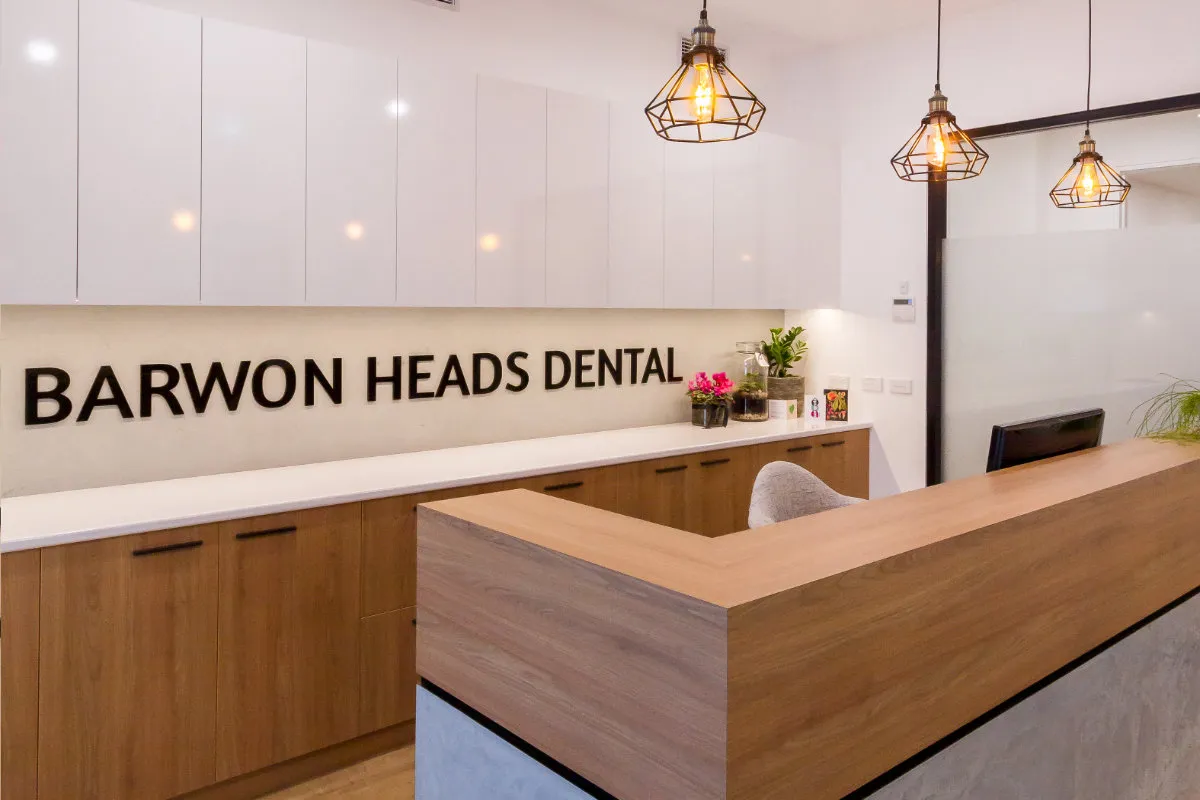 Reception desk with white upper cabinets, timber base cabinets, and BARWON HEADS DENTAL lettering on the splashback.
