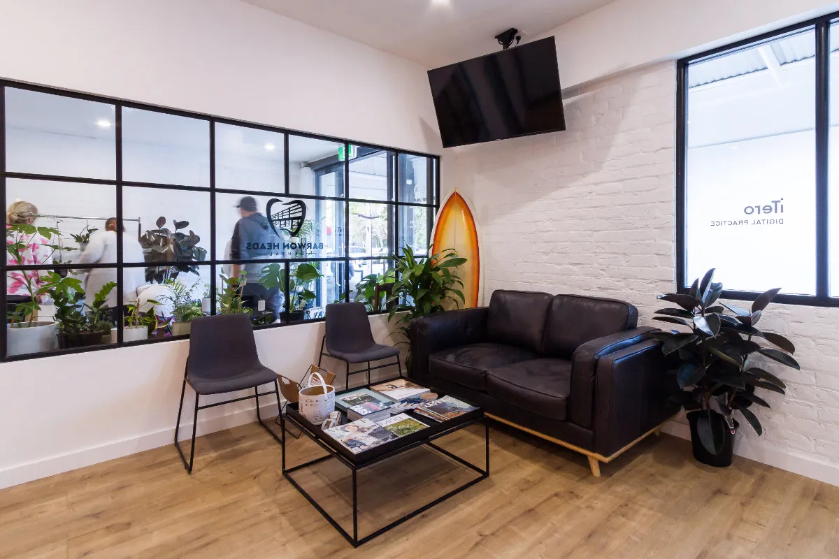 Patient waiting lounge with leather sofa, surfboard accent, and steel-framed glazed dividing wall.