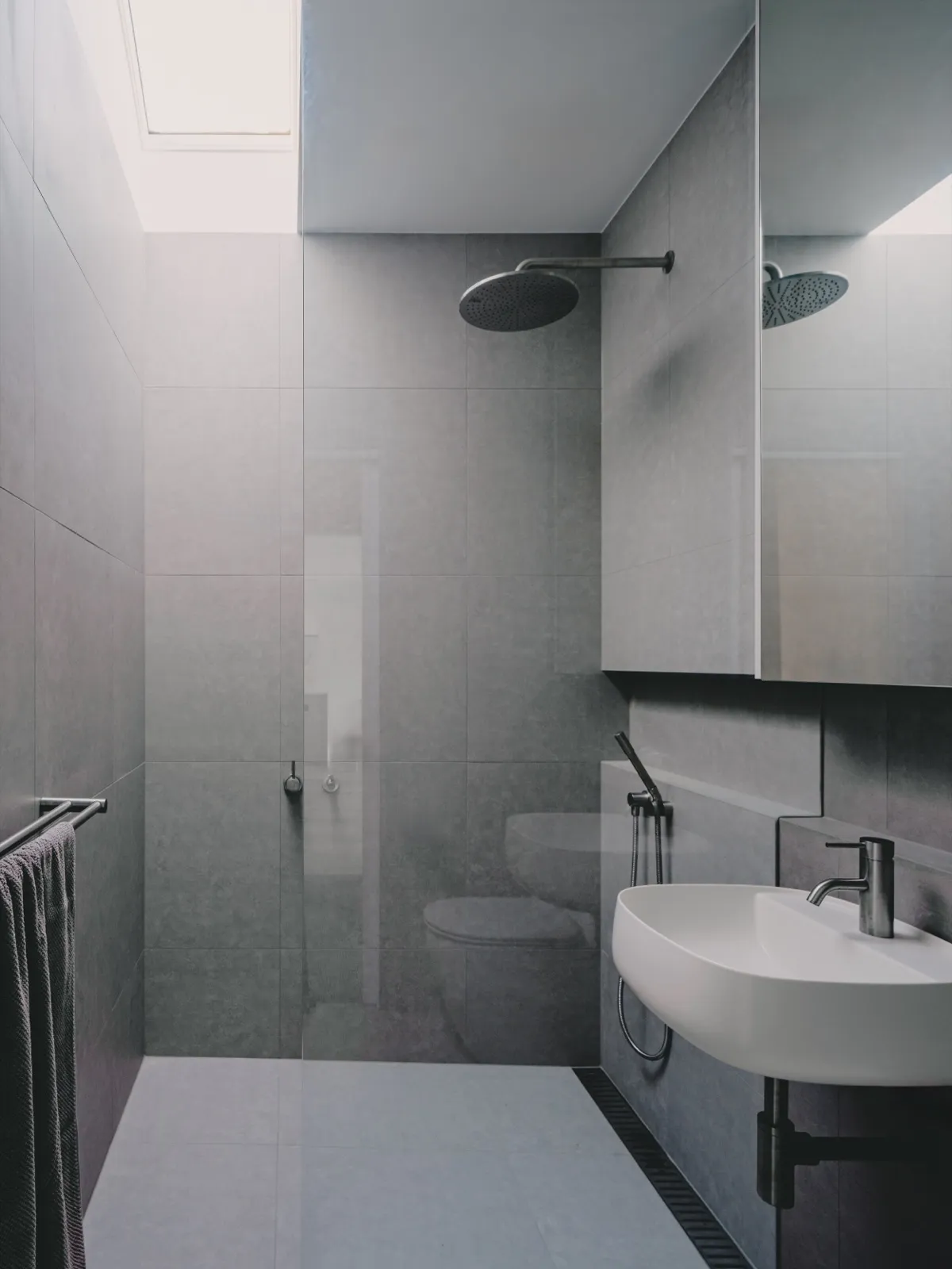 Grey-tiled ensuite with walk-in shower, rainfall and hand showers, mirrored cabinet, and a wall-hung white basin.