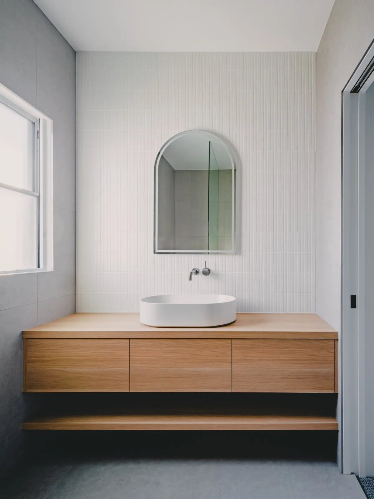 Powder room with timber floating vanity, round white basin, arched mirror, and a fluted feature wall.
