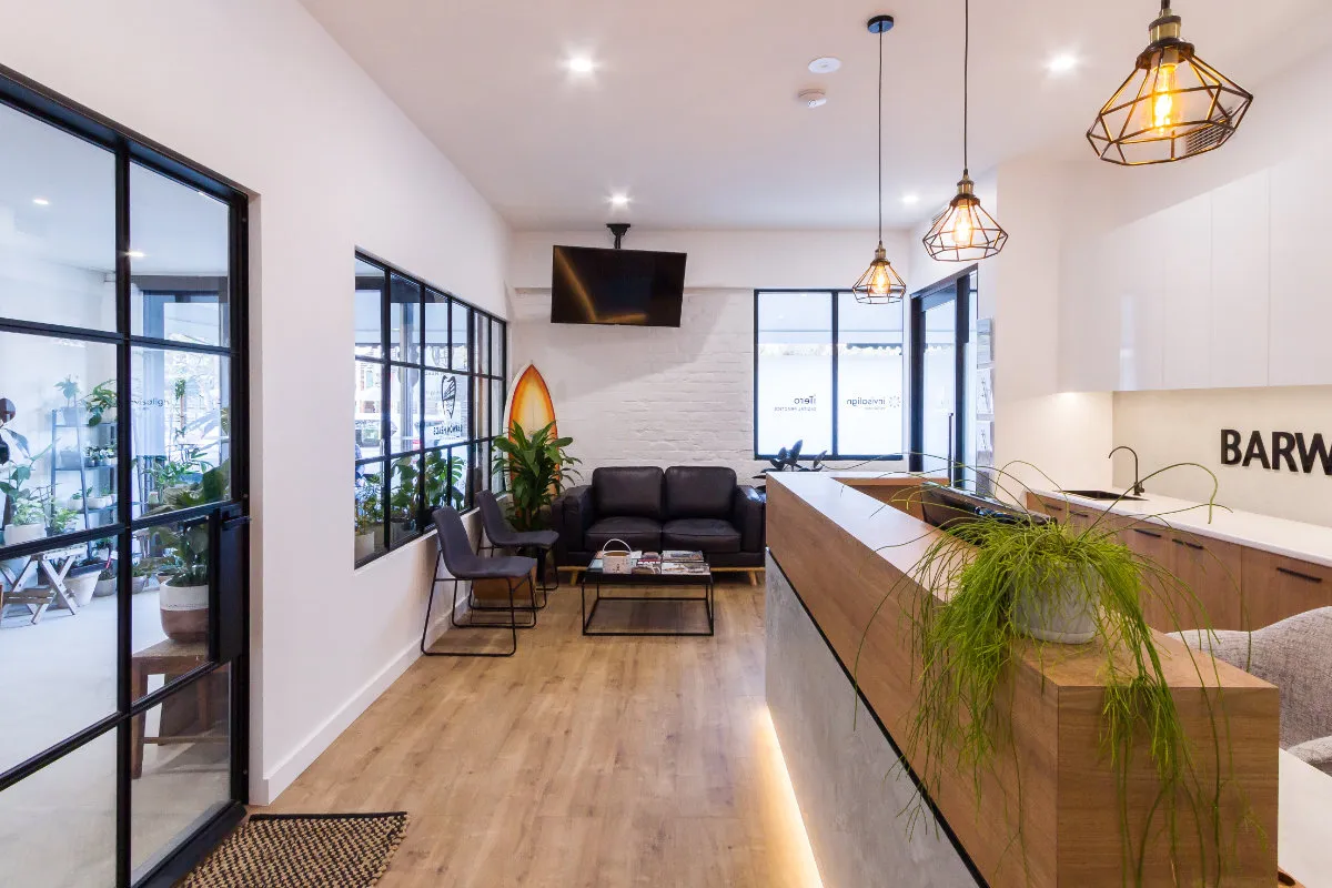 Open-plan waiting and reception space with pendant lights, leather sofa, and surfboard accent.