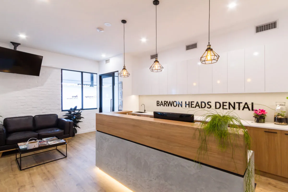 Reception view from the waiting lounge with three pendant lights above the desk and BARWON HEADS DENTAL signage.