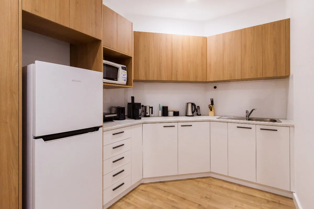 Staff kitchenette with timber upper cabinets, white base cabinets, and a stainless fridge.