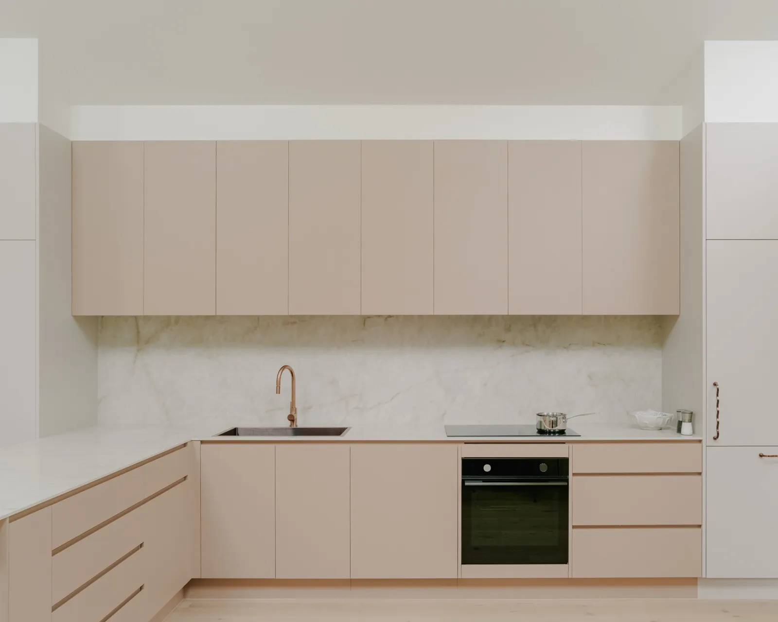 Galley butler's kitchen in blush cabinetry with marble splashback, brushed copper mixer, induction cooktop, and integrated under-bench oven.