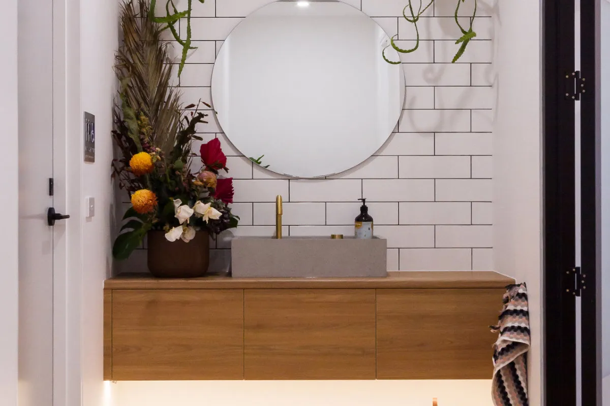 Powder room with round mirror, concrete vessel basin, white subway tiles, and a floral arrangement.