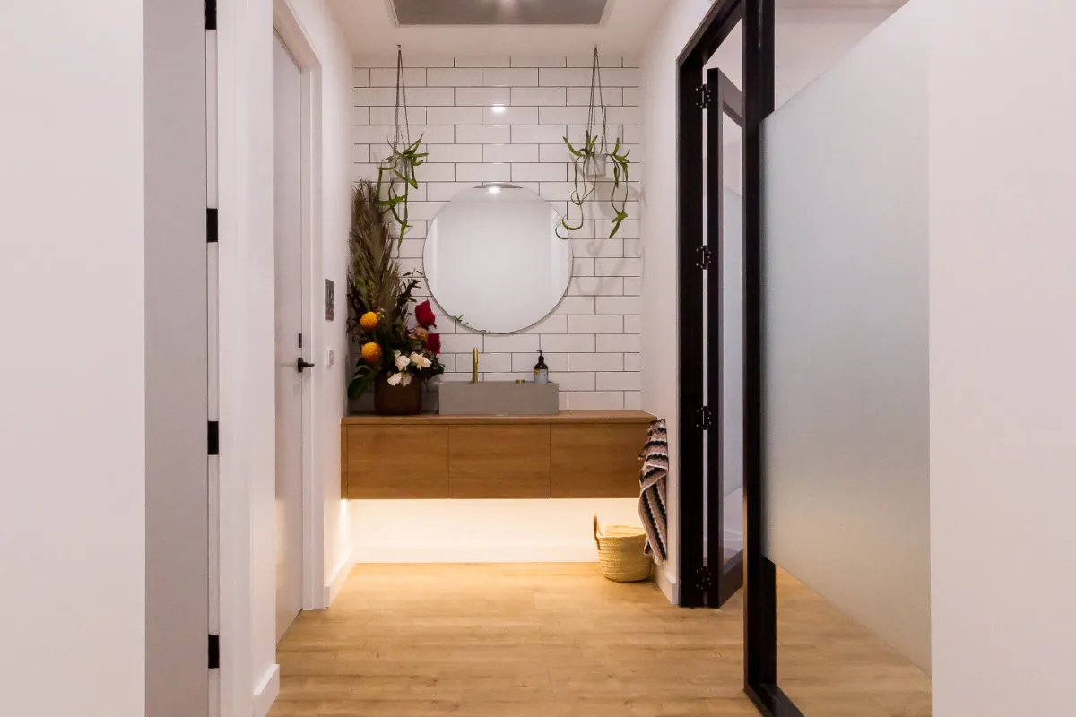 Corridor view through to the powder room with round mirror and timber vanity.