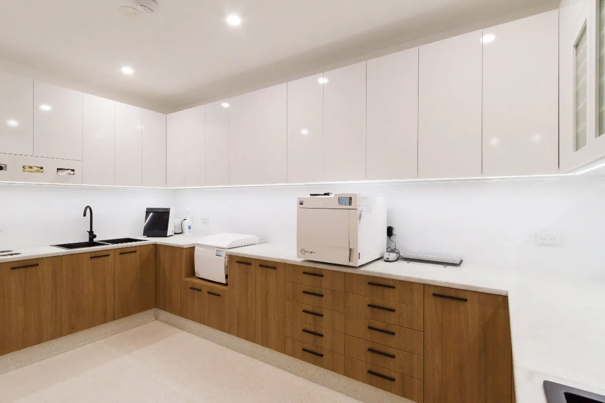Sterilisation room with stone benchtop, white cabinets, autoclave, and dental equipment.