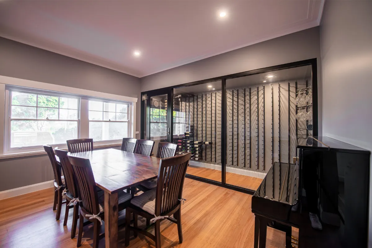 Formal dining room with timber table for eight, glass-fronted wine cellar, and upright piano.