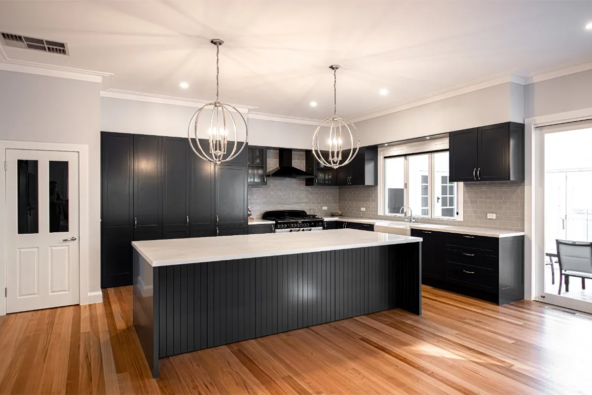 Hamptons-style kitchen with charcoal Shaker cabinets, twin polished-orb pendants, and timber flooring.