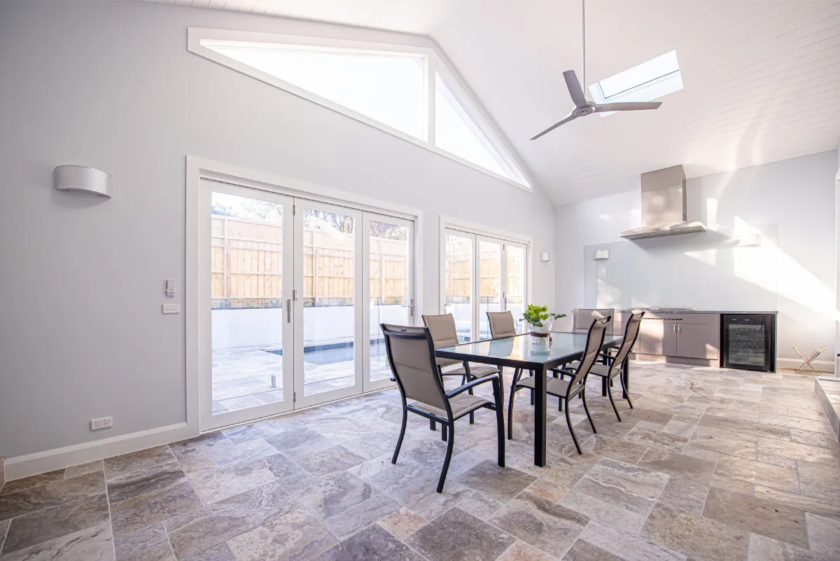 Alfresco dining room with vaulted ceiling, bifold doors to swimming pool, and travertine floor.