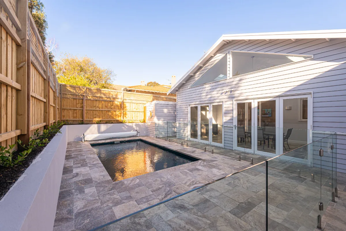 Backyard with plunge pool, glass balustrade, weatherboard rear facade, and stone paving.