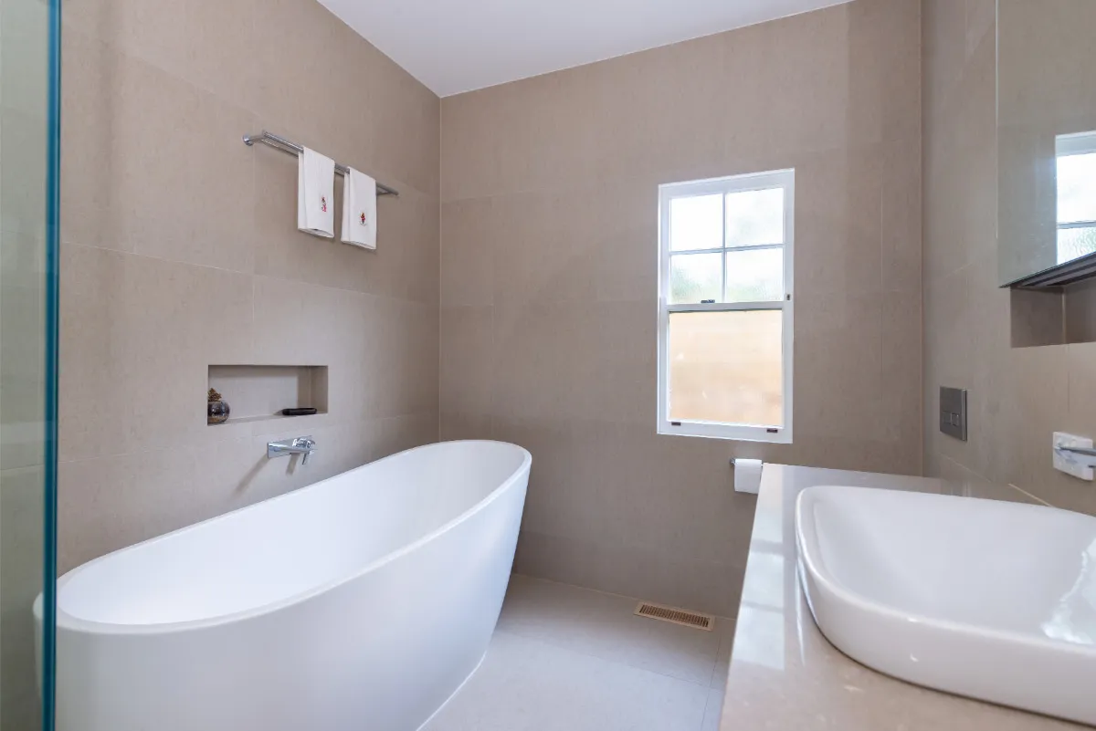 Renovated bathroom with freestanding tub, beige stone-look tiles, vessel basin, and frosted window.