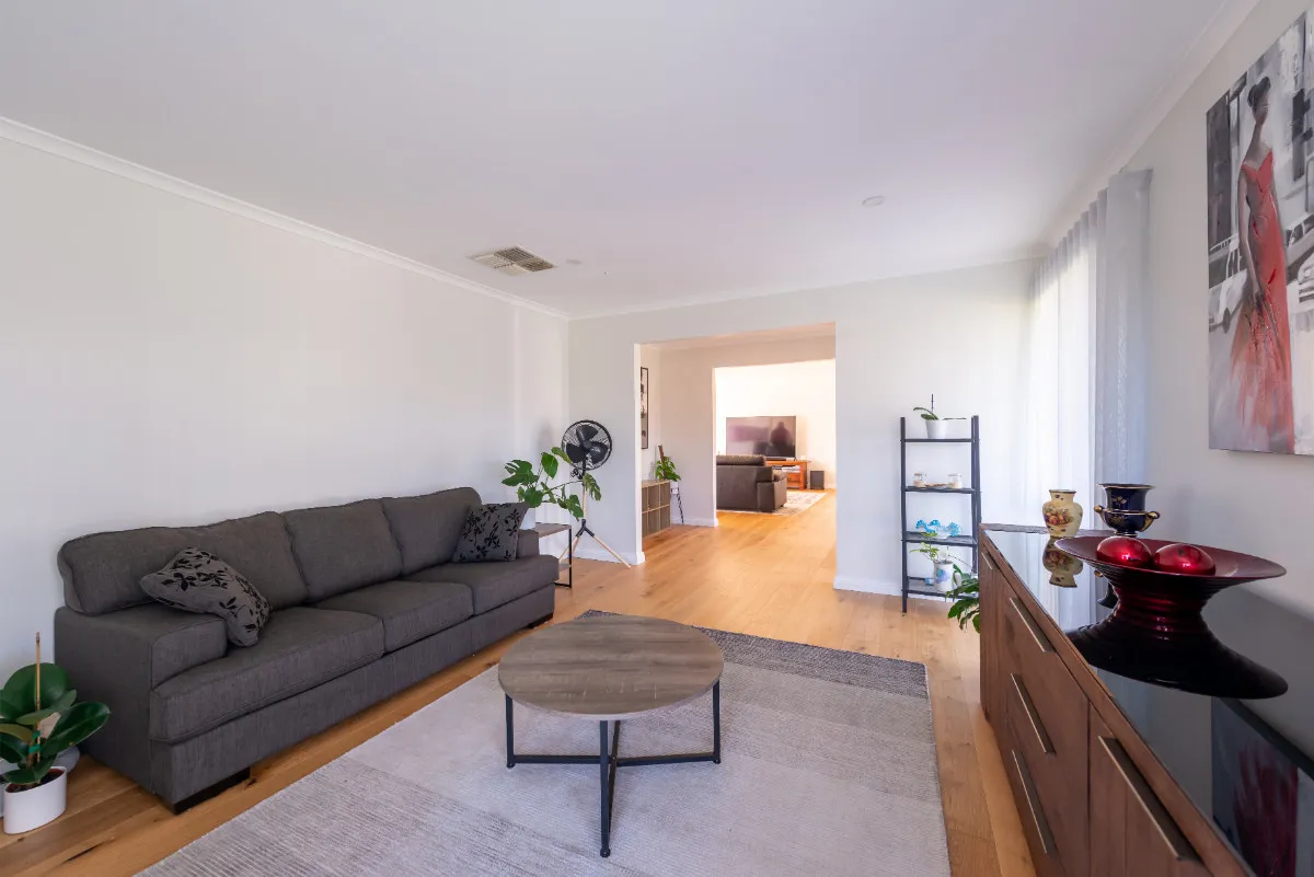 Open-plan living room with grey sofa, oak floor, vintage cabinet, and view through to a second living area.