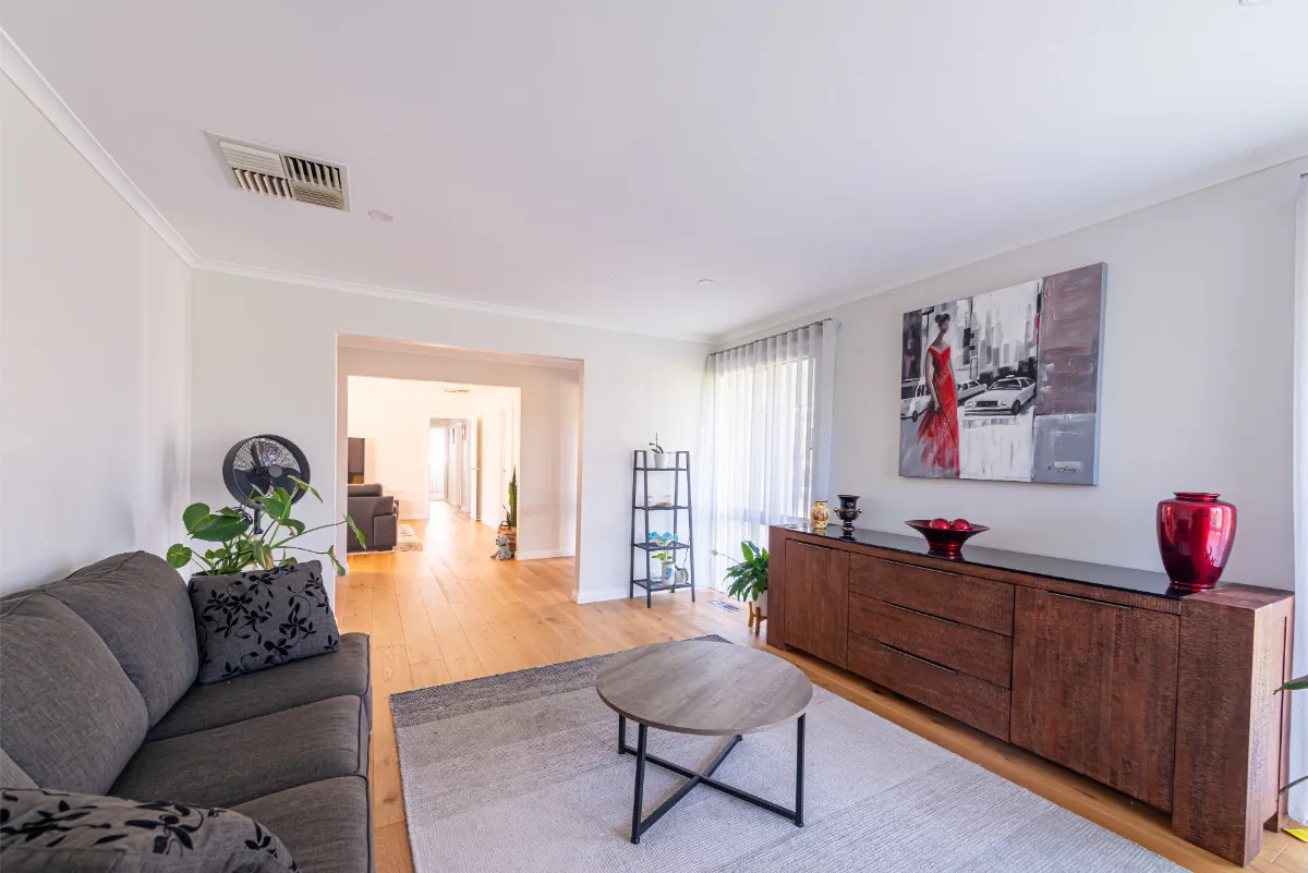 Lounge with grey sofa, dark timber sideboard with red vases, and a long internal corridor view.