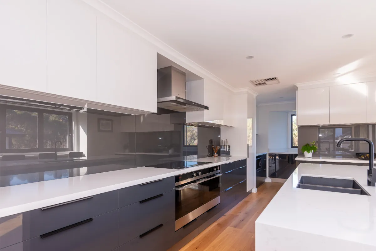 Galley kitchen with charcoal cabinets, white stone benchtops, induction cooktop, and oak flooring.