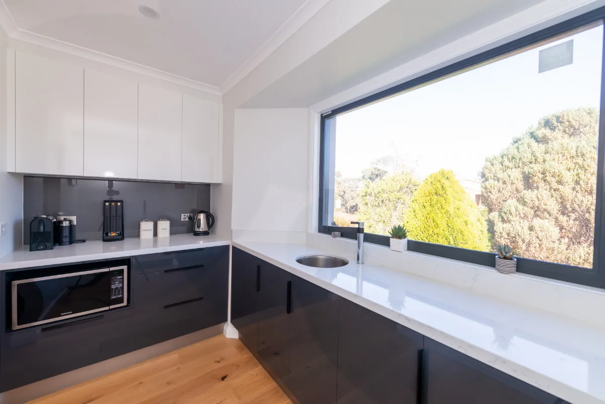 Butler's pantry with charcoal cabinets, microwave, white benchtop, and a large window over hedged garden.