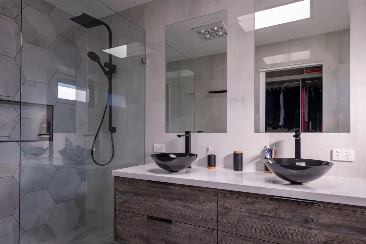 Bathroom with hexagonal feature tile, freestanding shower, twin black vessel basins, and timber vanity.
