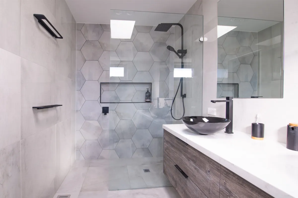 Walk-in shower with hexagonal grey tiles, recessed niche, matt-black tapware, and floating timber vanity.