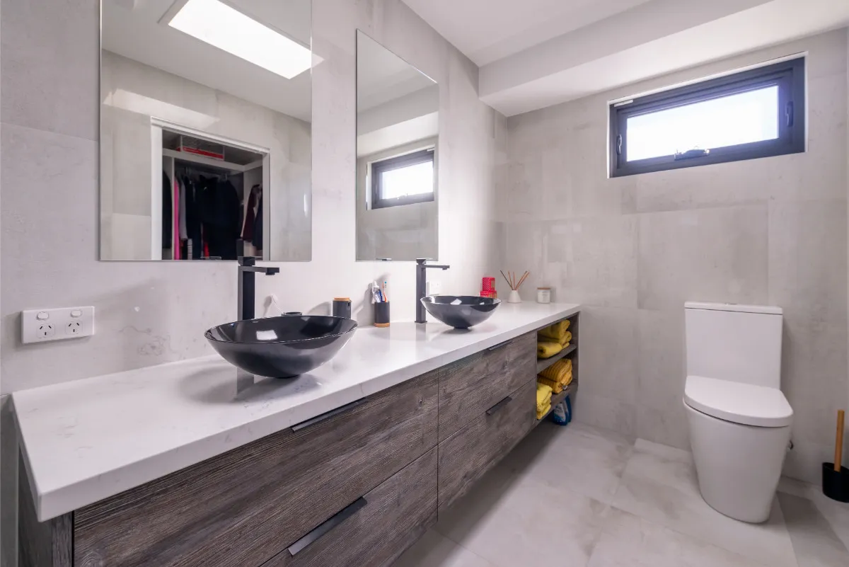 Twin black vessel basins on a timber vanity with mirrored cabinets and a toilet alcove.