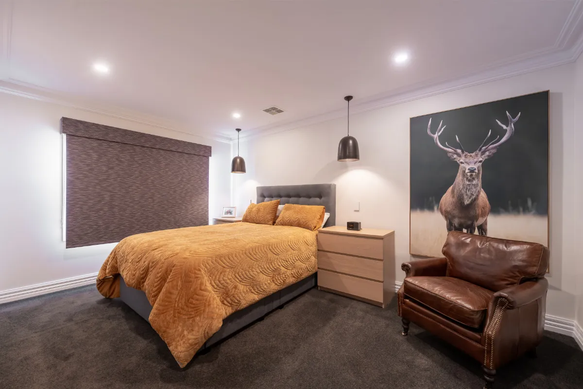 Master bedroom with king bed, gold quilted cover, leather armchair, and an oversized stag artwork.