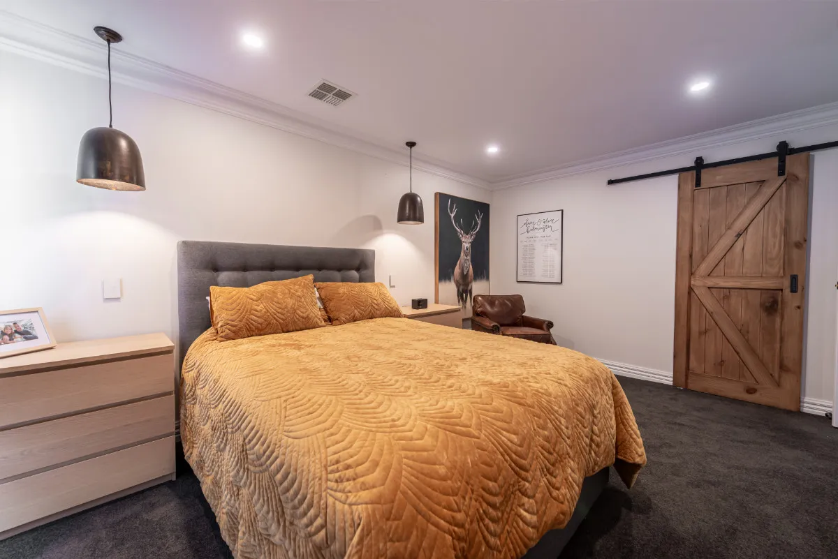 Master bedroom with sliding timber barn door, pendant lights, and a gold quilted king bed.