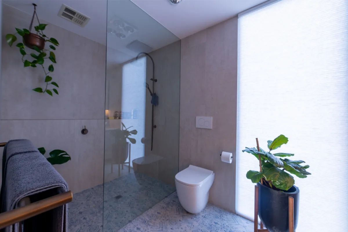 Wet-room ensuite with patterned floor tile, walk-in shower, wall-hung toilet, and indoor plants.