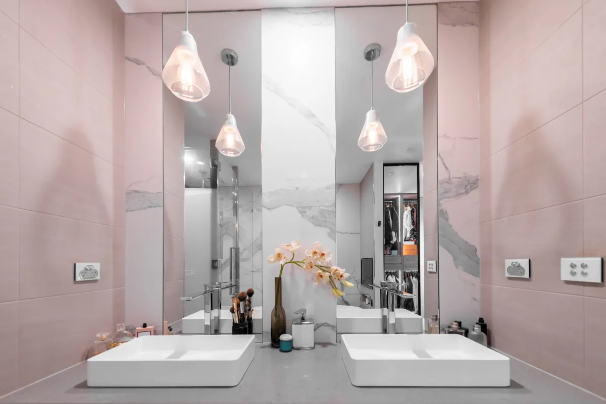 Powder room with pink tiled walls, marble feature panel, twin square vessel basins, and pendant lights.