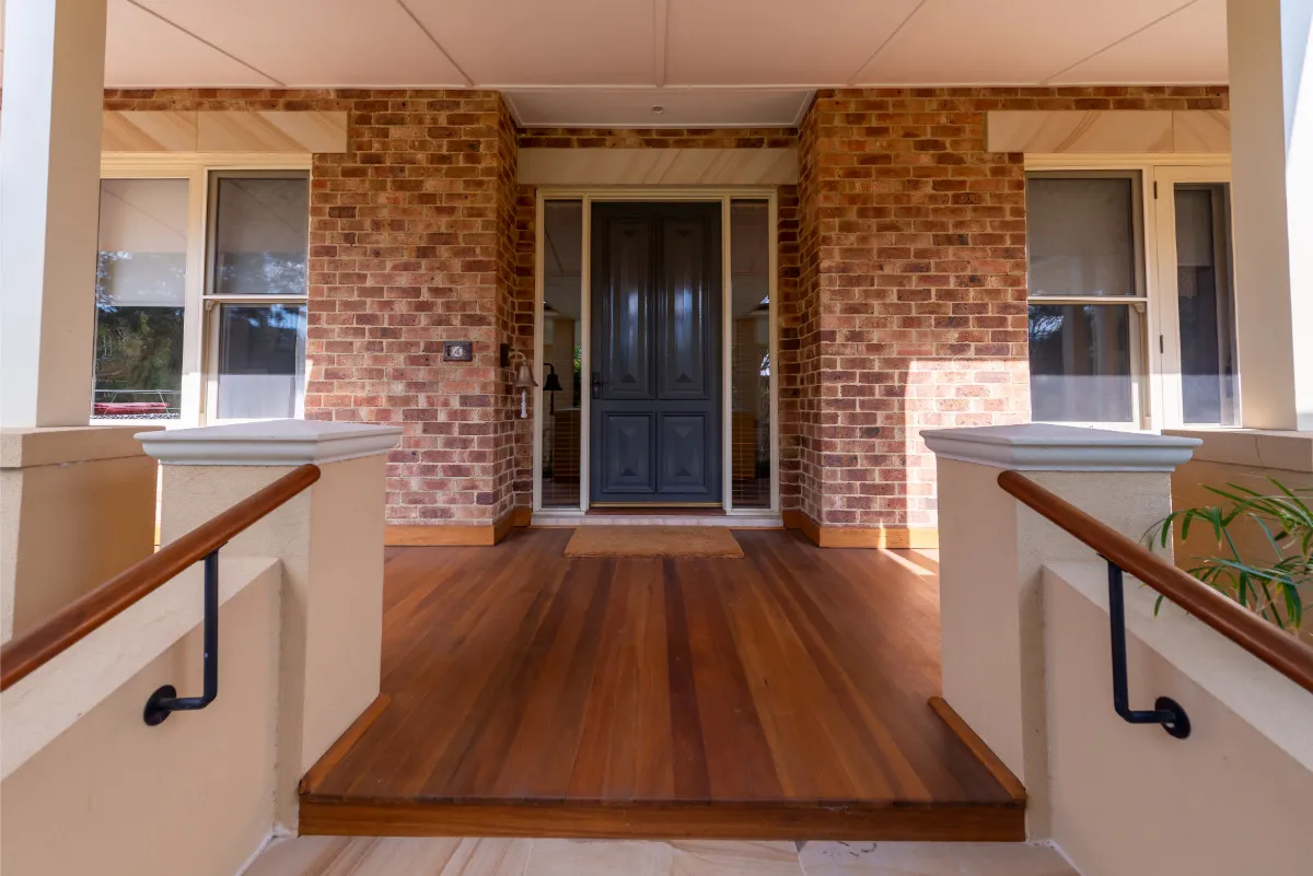 Front porch with brick piers, dark timber panelled door, decked entry, and rendered balustrades.