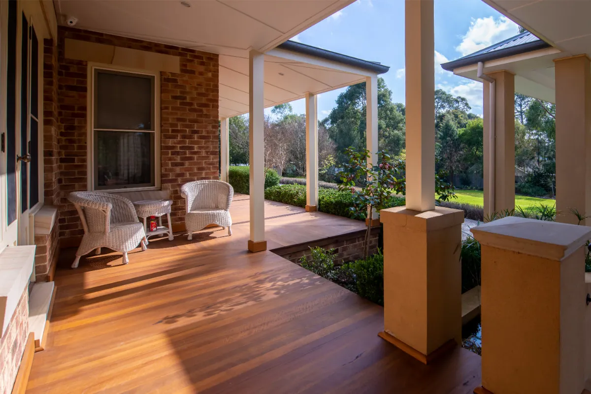 Wraparound timber verandah with brick columns, wicker seating, and hedged garden.
