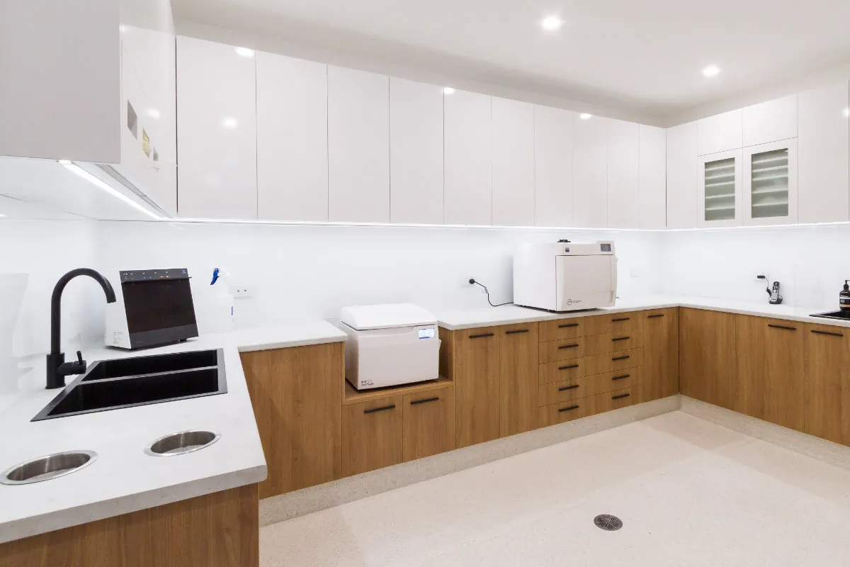 Sterilisation room with U-shaped joinery in white and timber, autoclave, and twin sinks.